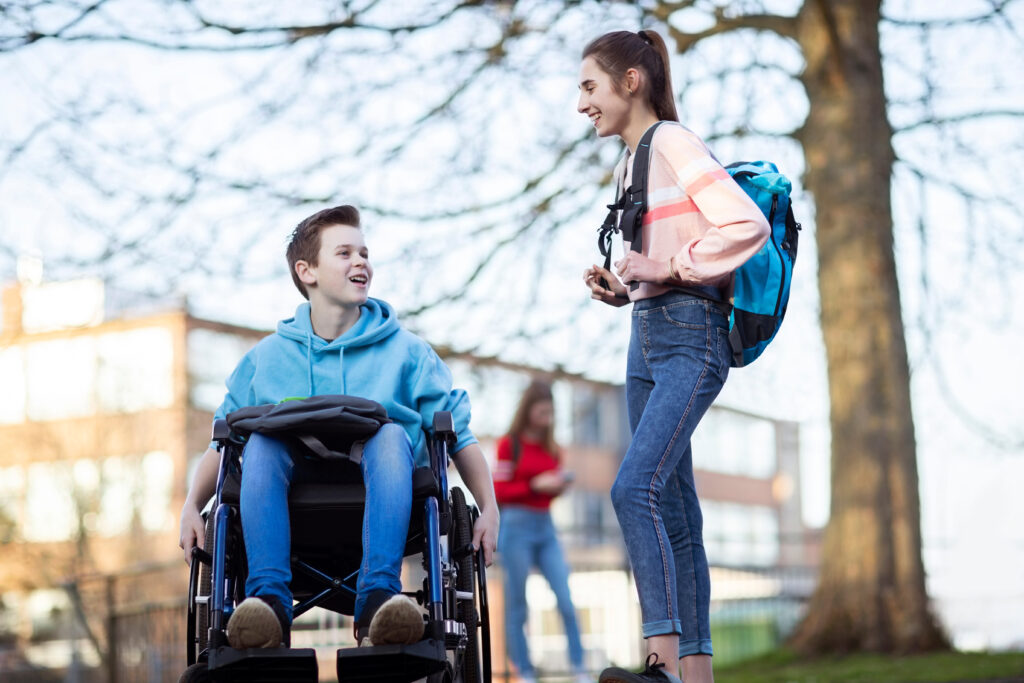 Adolescent en fauteuil roulant discutant avec une camarade de classe en entrant à l’école secondaire
