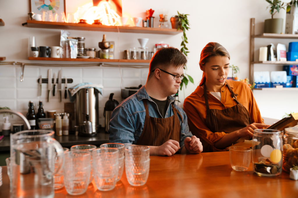 Femme accompagnant un jeune adulte en situation de handicap dans l’apprentissage de l'utilisation d’une machine en milieu de stage, favorisant l’autonomie et l’insertion dans la vie active.