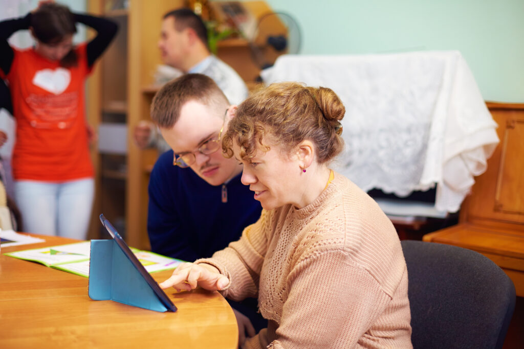 Un jeune adulte en situation de handicap et son éducatrice en centre de réadaptation, utilisant une tablette numérique dans le cadre de leur accompagnement vers la vie active.